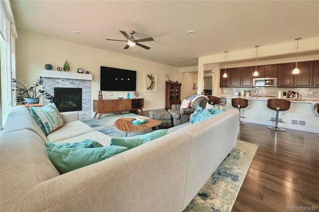 living room featuring ceiling fan, dark wood-type flooring, and a stone fireplace