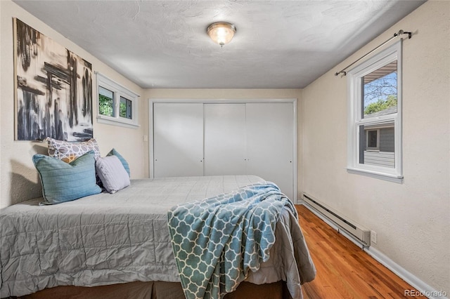 bedroom featuring a baseboard heating unit, hardwood / wood-style flooring, and a closet