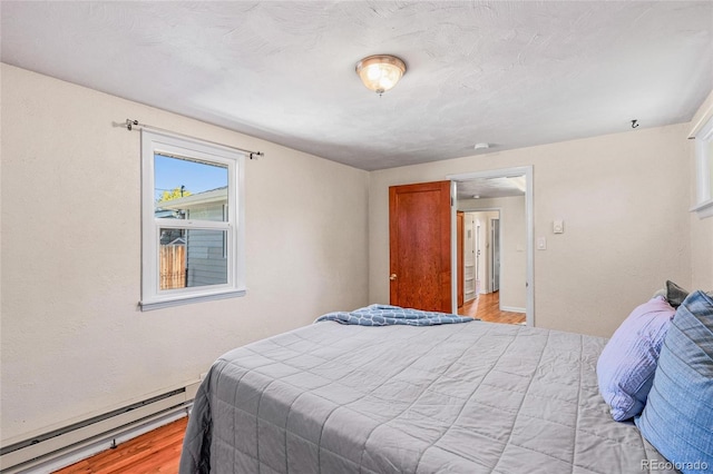 bedroom with a baseboard heating unit and light hardwood / wood-style flooring