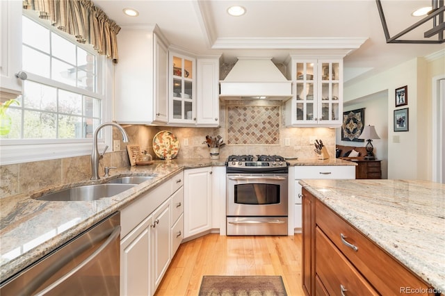 kitchen with stainless steel appliances, a sink, premium range hood, light wood-style flooring, and recessed lighting