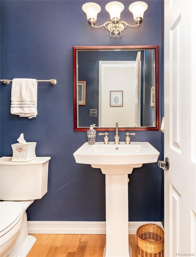 half bathroom with wood finished floors, baseboards, toilet, and a chandelier