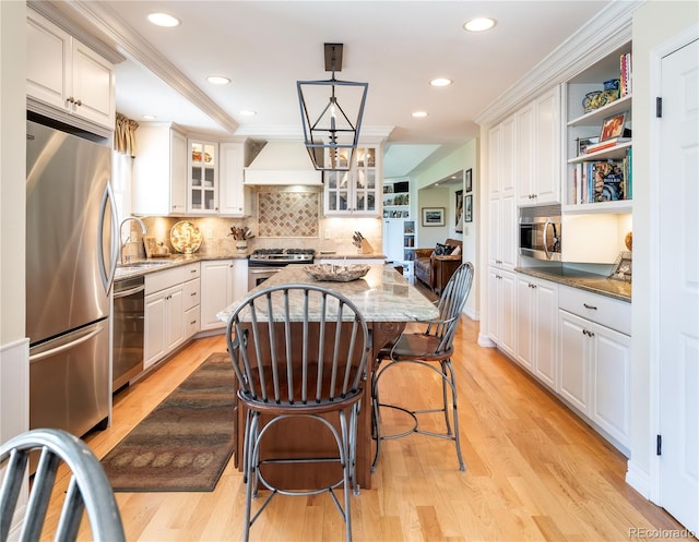 kitchen featuring stainless steel appliances, custom range hood, a kitchen island, light wood-style flooring, and light stone counters
