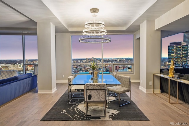 dining area with a notable chandelier, a tray ceiling, a view of city, and light wood-style floors