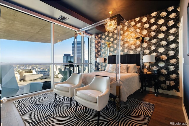 bedroom with baseboards, visible vents, wood finished floors, a wall of windows, and a city view