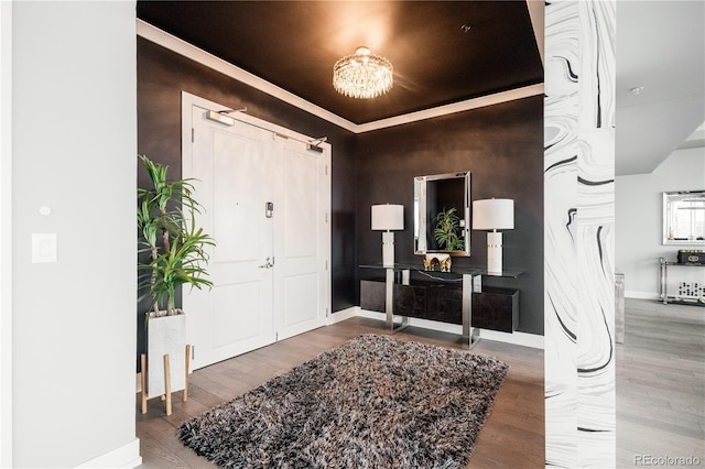 foyer with a raised ceiling, a notable chandelier, baseboards, and wood finished floors