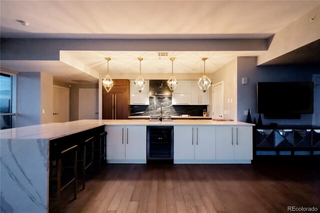 bar featuring hanging light fixtures, wall chimney range hood, wine cooler, and a sink