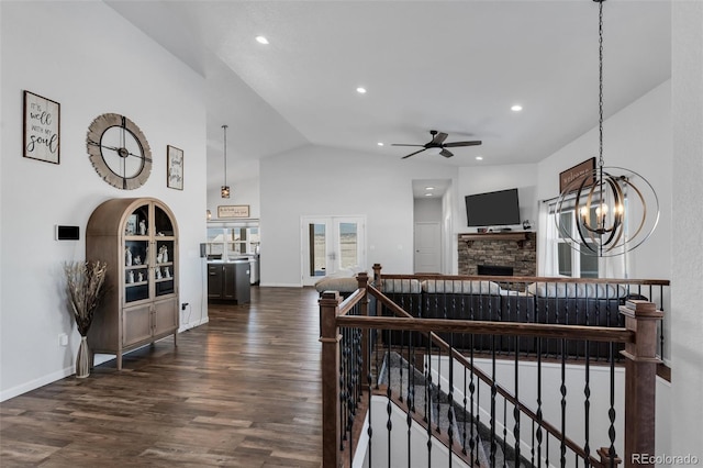 interior space featuring high vaulted ceiling, dark wood-type flooring, ceiling fan with notable chandelier, and a stone fireplace