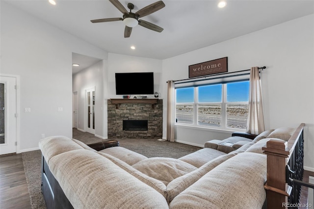 living room with ceiling fan, vaulted ceiling, dark wood-type flooring, and a stone fireplace