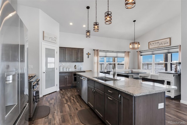 kitchen featuring decorative light fixtures, vaulted ceiling, dark brown cabinetry, a kitchen island with sink, and stainless steel appliances