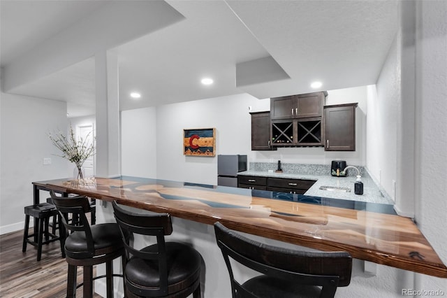 bar featuring stainless steel refrigerator, dark brown cabinets, sink, and hardwood / wood-style floors