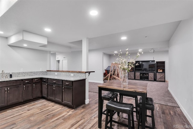 kitchen featuring kitchen peninsula, sink, light hardwood / wood-style flooring, light stone countertops, and dark brown cabinets