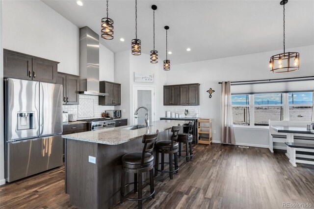 kitchen with appliances with stainless steel finishes, an island with sink, sink, dark brown cabinetry, and wall chimney range hood