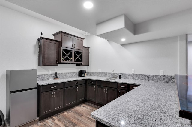 kitchen featuring sink, stainless steel refrigerator, dark brown cabinetry, kitchen peninsula, and light wood-type flooring