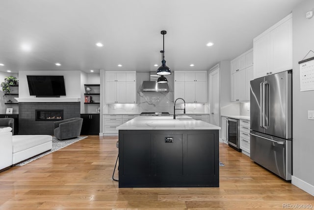 kitchen with high end refrigerator, a center island with sink, white cabinets, wine cooler, and light hardwood / wood-style floors