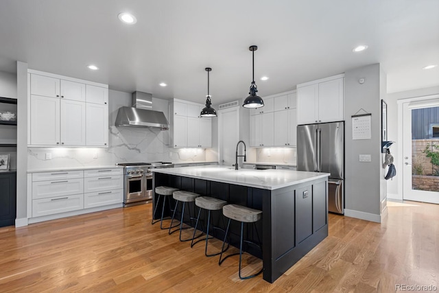 kitchen featuring a center island with sink, wall chimney range hood, light hardwood / wood-style flooring, premium appliances, and white cabinetry