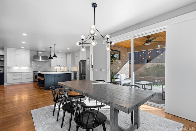 dining area featuring ceiling fan with notable chandelier, sink, and light hardwood / wood-style flooring