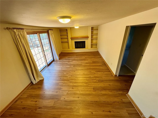 280 Raven Hills Rd, Colorado Springs, CO 80919 - unfurnished living room with a textured ceiling, built in features, a brick fireplace, wood finished floors, and baseboards