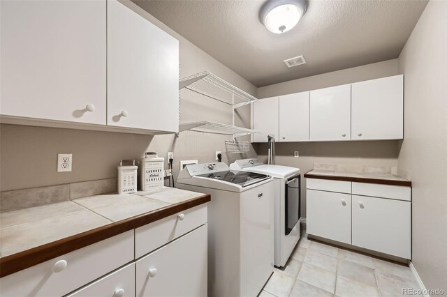 laundry area with visible vents, washing machine and clothes dryer, cabinet space, light tile patterned floors, and baseboards