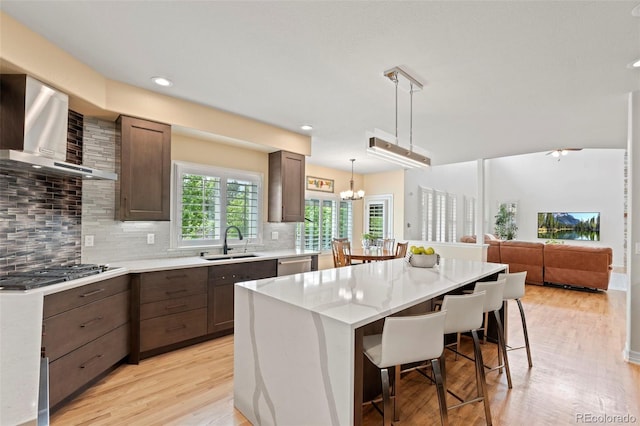 9468 E Aspen Hill Ln, Lone Tree, CO 80124 - kitchen featuring wall chimney exhaust hood, appliances with stainless steel finishes, a kitchen island, light countertops, and light wood finished floors
