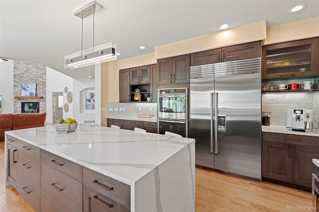 9468 E Aspen Hill Ln, Lone Tree, CO 80124 - kitchen with appliances with stainless steel finishes, tasteful backsplash, glass insert cabinets, light wood finished floors, and dark brown cabinetry