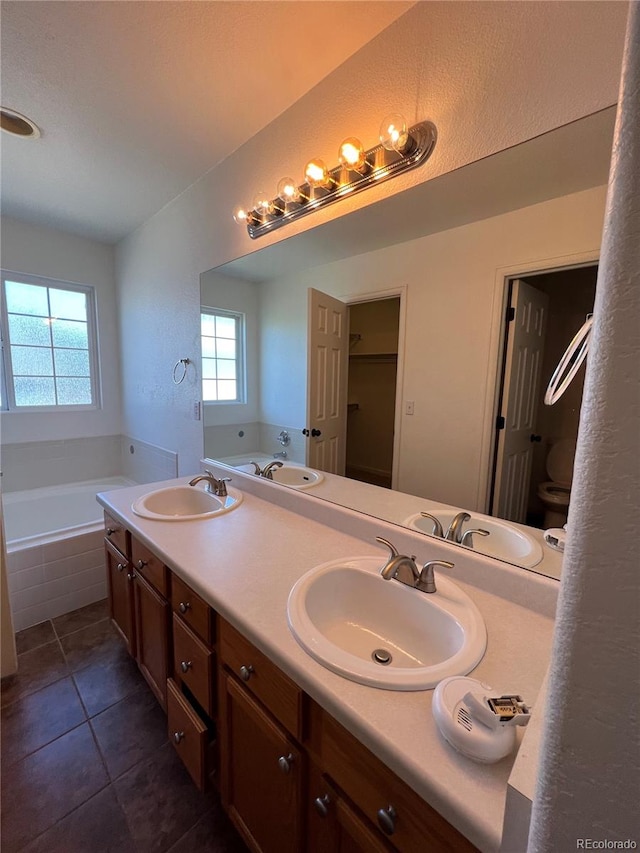 bathroom with tile patterned flooring, tiled tub, vanity, and toilet