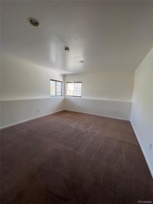 empty room with a textured ceiling, vaulted ceiling, and dark colored carpet