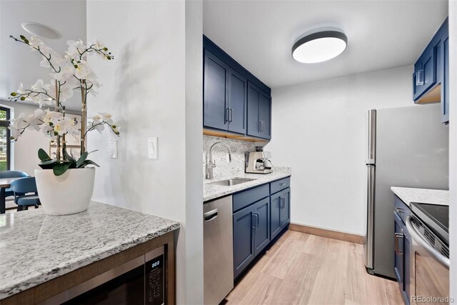 3131 E Alameda Ave Unit 803, Denver, CO 80209 - kitchen with appliances with stainless steel finishes, blue cabinetry, light wood finished floors, tasteful backsplash, and light stone counters