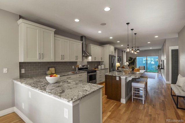 kitchen with wall chimney exhaust hood, decorative light fixtures, a center island, stainless steel appliances, and light stone countertops