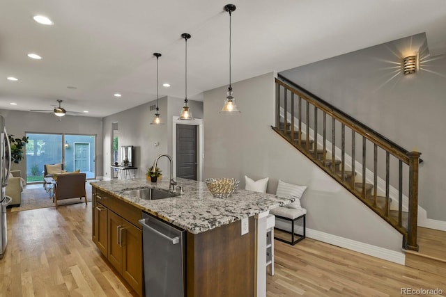 kitchen with decorative light fixtures, dishwasher, sink, light hardwood / wood-style floors, and a center island with sink