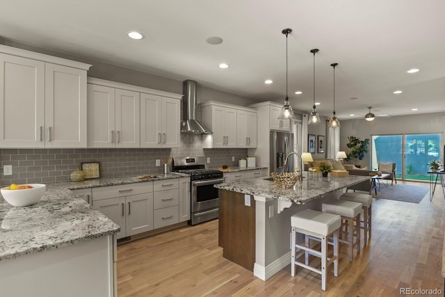 kitchen with appliances with stainless steel finishes, a center island with sink, a kitchen bar, and wall chimney exhaust hood