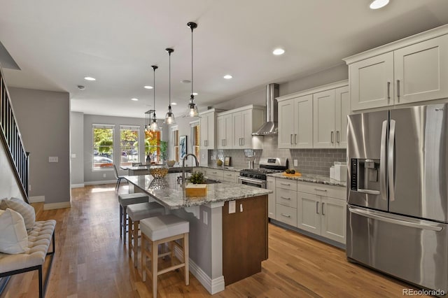 kitchen with sink, decorative light fixtures, stainless steel appliances, light stone countertops, and wall chimney range hood