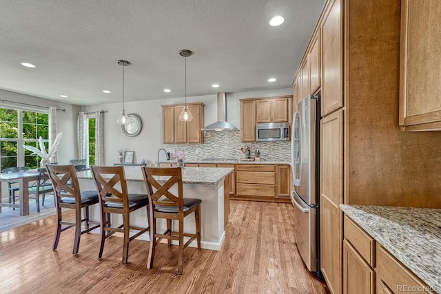 15235 W Iliff Ave, Lakewood, CO 80228 - kitchen with wall chimney range hood, appliances with stainless steel finishes, a kitchen bar, light wood-style floors, and decorative backsplash