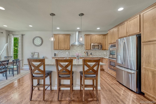 15235 W Iliff Ave, Lakewood, CO 80228 - kitchen featuring appliances with stainless steel finishes, wall chimney exhaust hood, light wood finished floors, tasteful backsplash, and an island with sink