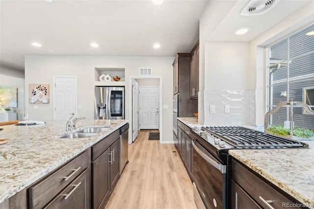 kitchen with sink, dark brown cabinets, light hardwood / wood-style flooring, appliances with stainless steel finishes, and light stone countertops