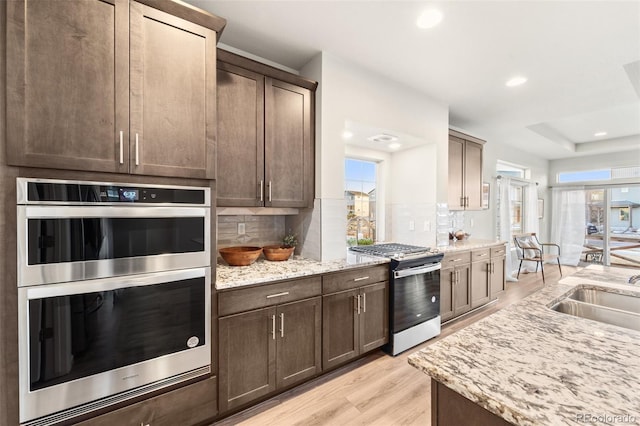 kitchen with sink, backsplash, stainless steel appliances, light hardwood / wood-style floors, and light stone countertops