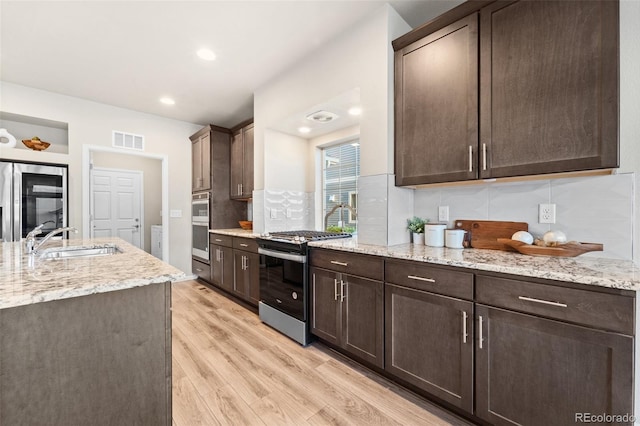 kitchen with sink, appliances with stainless steel finishes, dark brown cabinets, light stone counters, and light wood-type flooring