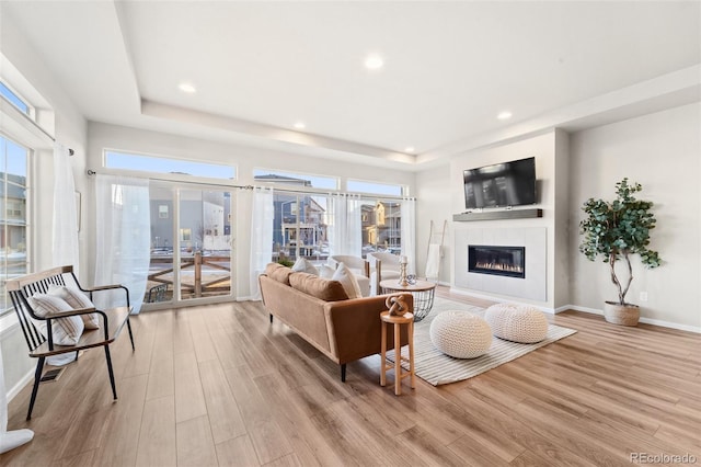 living room featuring a tiled fireplace, a tray ceiling, and light hardwood / wood-style floors