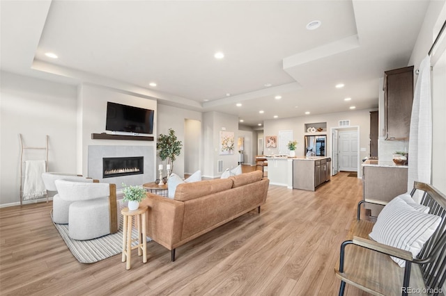 living room featuring a raised ceiling, a fireplace, and light hardwood / wood-style flooring