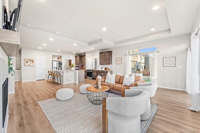 living room with a tray ceiling and light wood-type flooring