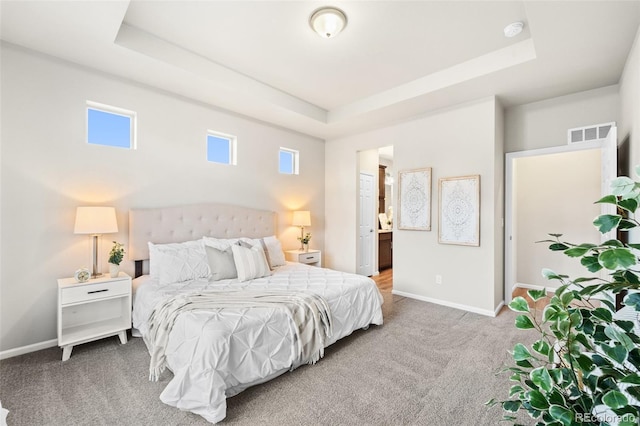 bedroom with multiple windows, carpet floors, ensuite bath, and a tray ceiling