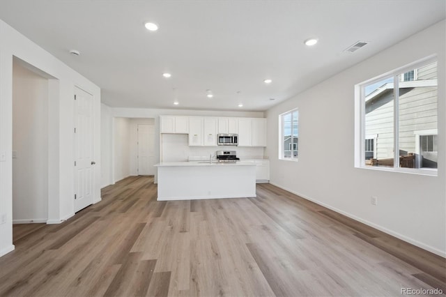 kitchen featuring sink, light hardwood / wood-style flooring, an island with sink, white cabinets, and appliances with stainless steel finishes