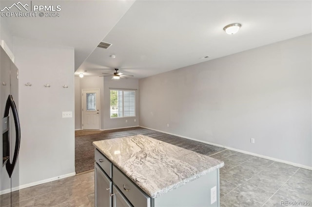 kitchen with light stone countertops, a center island, ceiling fan, and stainless steel refrigerator with ice dispenser