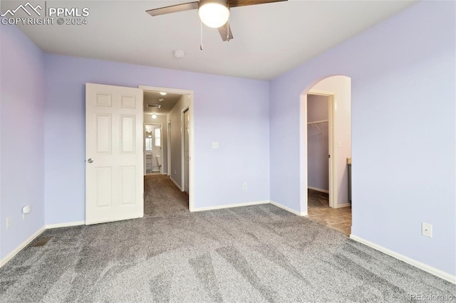 unfurnished bedroom featuring carpet, ceiling fan, a walk in closet, and a closet