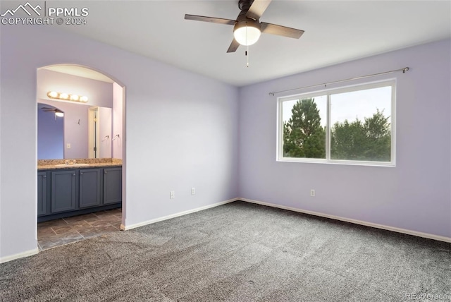 unfurnished bedroom with ceiling fan, dark carpet, sink, and ensuite bath