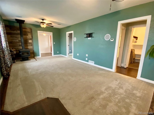 unfurnished living room featuring ceiling fan, a wood stove, and carpet floors