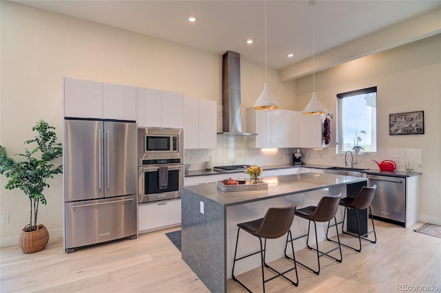 5125 W 29th Ave Unit 1, Denver, CO 80212 - kitchen featuring appliances with stainless steel finishes, wall chimney exhaust hood, a kitchen breakfast bar, light wood-style floors, and a kitchen island
