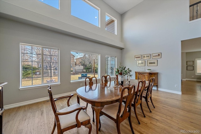 dining space with light wood-type flooring, a towering ceiling, a wealth of natural light, and baseboards