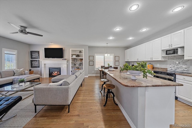 kitchen with light stone counters, a breakfast bar, white cabinets, open floor plan, and light wood-type flooring