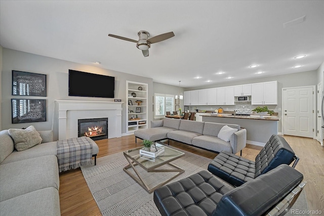 living room featuring recessed lighting, light wood-style floors, a glass covered fireplace, ceiling fan, and baseboards