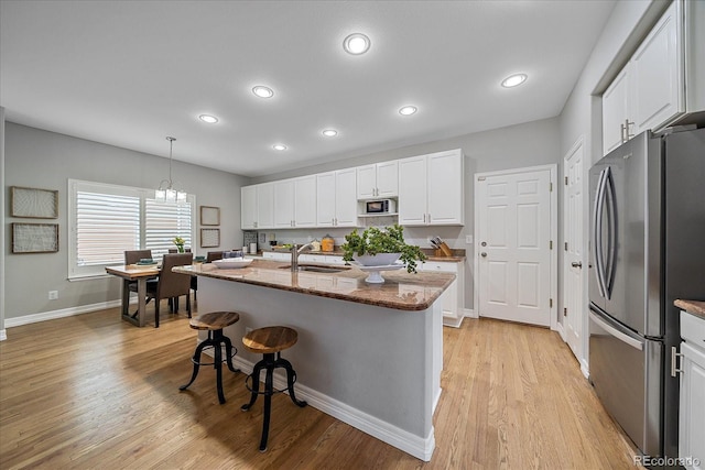 kitchen with white cabinets, freestanding refrigerator, a kitchen bar, black microwave, and a sink